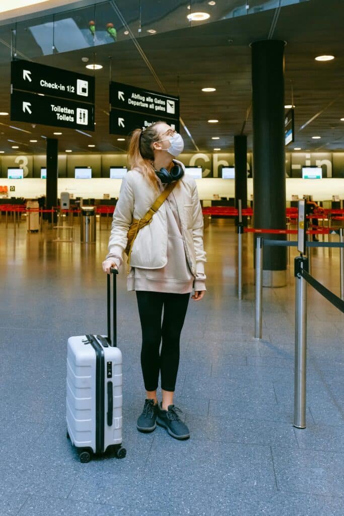 A woman in a face mask stands with her luggage in an empty airport terminal